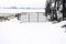 Rustic metal gate and fence locked by the entrance of a vast snow covered farm field in winter