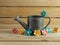 Rustic metal watering can surrounded by felt flowers on a real wood background.  Pink, yellow and blue felt flowers.  Country