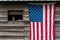 Rustic outside wall of wood building with green metal roof, open window with dusty lantern on windowsill, American flag hanging on