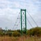 Rustic steel suspension bridge over the river. Overcast autumn morning