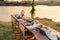 Rustic style dining table with flower, wine glass, candle decoration at dinner by the river in the sunset