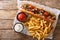 Rustic style hot dog with bacon and vegetables served with french fries and sauces close-up. horizontal top view