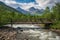 rustic wooden bridge over rushing river, with majestic mountains in the background