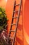 Rustic wooden ladder against a bright orange wall