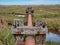 A rusting drainage pipe on weathered wooden supports at Stiffkey Salt Marshes on the North Norfolk Coast Path.