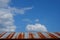 Rusting tin roof of a barn against a beautiful blue sky with puffy white clouds