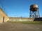 Rusting water tower stands beyond the wall and bard wire fence