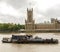 A rusty boat parked in brown waters of Thames river in front of scenic Houses of Parliament