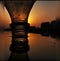 A rusty bottle reflection on water with a sunset creating a silhouette effect and shadows