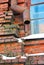 Rusty drain pipe along window corner on red brick wall, snow on window sill