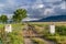 Rusty gate chain link fence and dirt road on a grassy field in front of a lake