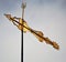 Rusty, gold weather vane against a cloudy blue sky