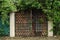 Rusty metal garage surrounded by green grass, brick wall with a wall of green leaves