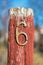 Rusty number six on a red wooden pole at the entrance of an house