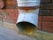 Rusty old metal downspout on blurred red brick wall. Gutter pipe. Water shoot. Downpipe on building facade background. Housing and