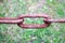 Rusty oxidized brown link of old ancient strong strong wrought iron metal chain against the background of green