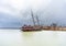 Rusty shipwreck marooned near shore on lake under a stormy blue