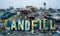 Rusty signage spelling LANDFILL towers over a pile of discarded vehicles and waste, a stark symbol of environmental concerns