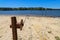 A rusty wench with a long cable in the silky brown sand of the beach on the banks of the rippling lake with lush green treeys