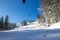 It`s a beautiful sunny day on the mountain. View of the ski lift and the ski slope full of cross-country skiers. There are pine