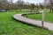 S-shaped winding wooden walkway bridge over green grass with hiking trail signs