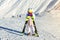 Sad adorable preschooler caucasian tired kid girl resting leaning on ski in helmet, goggles and unicorn fun costume