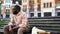 Sad african man sitting lonely on city bench with flower bouquet, failed date