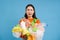 Sad asian female student, holds recycling waste, collects plastic garbage to take it to recycle center, blue background