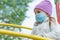 Sad baby girl played on the playground outside, wearing medical mask, protecting his face from polluted airborne dust