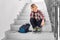 Sad blond boy sitting on stairs in corridor of school.