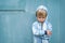 Sad bored resentful child boy in hoodie standing near blue wall. Cute upset distressed kid pouts his lips. Emotional portrait