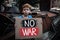 Sad boy holding poster No War near broken military tank outdoors