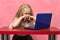 sad, brooding schoolgirl behind the laptop. pink background.
