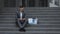 Sad businessman sitting on stairs outdoor with box of personal office stuff. Despaired male lost work place and looking