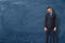 Sad businessman in suit standing with bowed head and arms down near the blue chalkboard