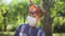 Sad Caucasian teenage redhead boy in coronavirus face mask and party hat in sunrays outdoors alone on birthday. Portrait