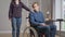 Sad depressed disabled man in wheelchair thinking as unrecognizable woman putting hand on shoulder in slow motion