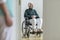 Sad disabled elderly man in the wheelchair in the hospital. Blurred nurse in a foreground