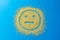 Sad emoji smile on a blue background. Smiley from yellow sugar grains.