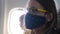 Sad female flight passenger in dark blue face mask fly in airplane