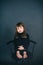 Sad and frustrated little girl with long hair in a black clothes and barefoot sits on a chair in the studio