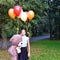 Sad girl child hugs a big teddy bear and balloons in the park. Schoolgirl unhappy in the park with a big toy and balls