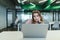 A sad girl with a cup of coffee in her hands uses a laptop on the desk in the office