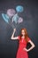 Sad girl holding drawn colorful balloons over blackboard background