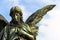 Sad guardian angel bronze sculpture with open long wings across the frame against a bright blue white sky.