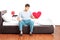 Sad guy sitting alone on bed and holding a heart