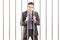 Sad handcuffed businessman in suit posing in jail and holding ba