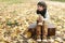 Sad little boy sitting on suitcase in the autumn park