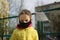 Sad little girl in face mask in yellow jacket standing near closed playground outdoor. Kids play area locked because of
