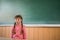 Sad little girl standing near the blackboard. Baby doesn`t want to go to school. A child does not have a assignment. School